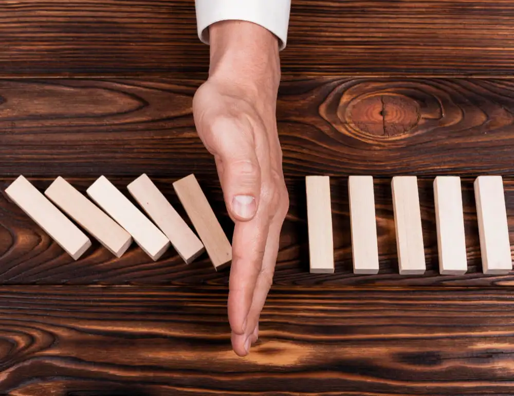 Hand stopping a line of falling dominoes on a wooden surface, symbolizing proactive risk management and business continuity planning.