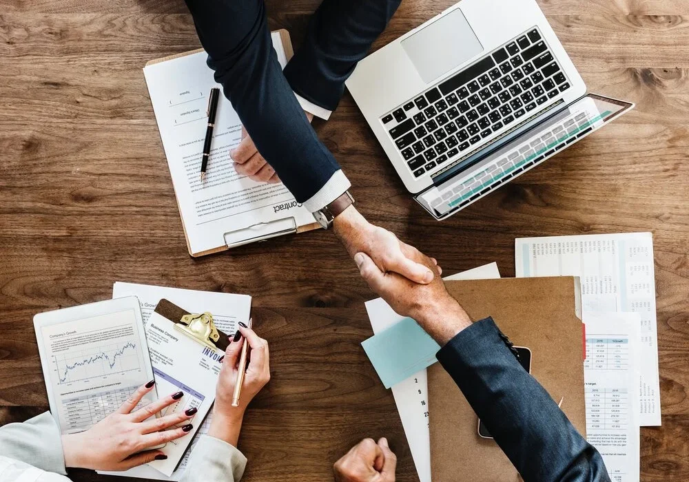 Business meeting with handshake, documents, and laptop, symbolizing partnerships in the countries we operate in across global markets.